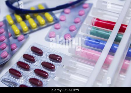 Diverses pilules colorées et tubes à essai disposés sur une table de laboratoire avec des verres Banque D'Images