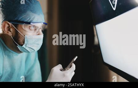 Chirurgien jetant un coup d'œil au téléphone à côté d'une radiographie éclairée Banque D'Images