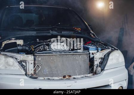 Voiture avec son capot ouvert révélant le moteur dans un environnement brumeux par faible luminosité Banque D'Images