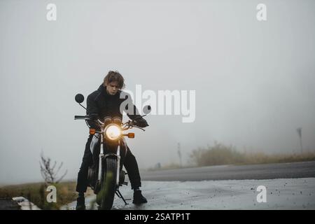 Une personne sur une moto navigue sur une route brumeuse, créant un sentiment de solitude et d'aventure Banque D'Images
