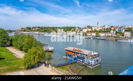 La Sava traverse Belgrade, avec ses cafés animés et sa végétation luxuriante. Les gens apprécient les activités de loisirs le long des berges tandis que les bateaux naviguent sur l'eau. Banque D'Images