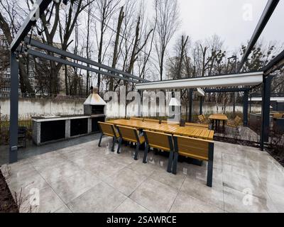 Patio extérieur tendance pergola structure d'ombre, auvent et toit de patio, table à manger, chaises, grill en métal entouré par l'aménagement paysager Banque D'Images