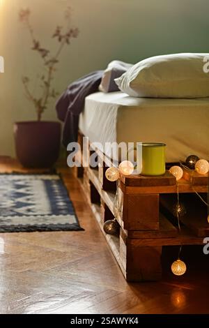 Scène matinale confortable dans une chambre avec tasse à café sur un lit de palette avec des lanternes Banque D'Images