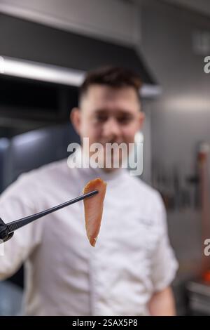 Chef professionnel montrant une tranche parfaite de poisson fumé, démontrant l'expertise culinaire dans une cuisine de restaurant moderne Banque D'Images