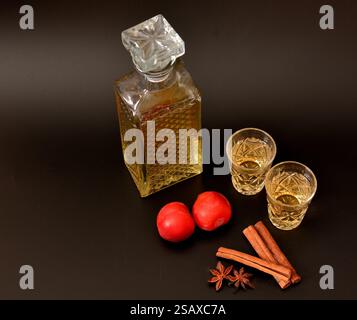 Liqueur de prunes aux épices sur fond noir, alcool maison dans une carafe en cristal et deux verres, fruits mûrs, anis et cannelle. Gros plan. Banque D'Images