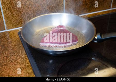 Tranche de steak de thon frais cru assaisonné cuite dans une poêle en aluminium. Gros plan, pas de gens. Banque D'Images