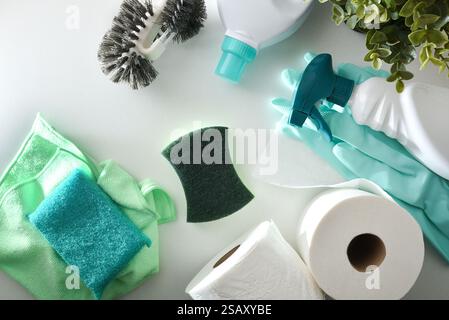 Fournitures de nettoyage de salle de bain telles que des bouteilles de désinfectant, des tampons à récurer, des gants, une brosse de toilette et du papier toilette sur une table en bois blanc. Vue de dessus. Banque D'Images
