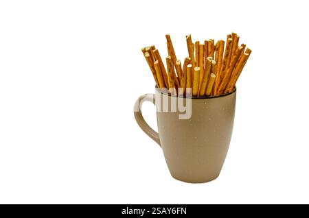 Un gros plan d'une collection de bâtonnets de bretzel brun doré soigneusement disposés à l'intérieur d'un mug en céramique beige. Banque D'Images