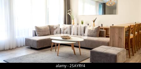 Salon moderne avec canapé gris, table basse blanche, coin repas en bois et lumière naturelle Banque D'Images