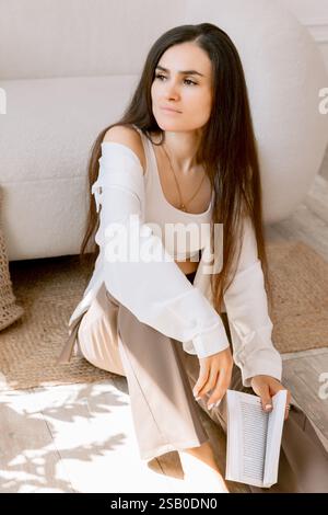 Portrait de femme élégante avec de longs cheveux tenant un livre dans un cadre intérieur confortable Banque D'Images