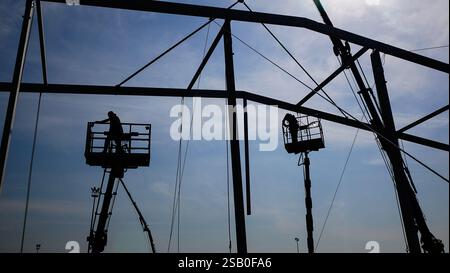 Les travailleurs de l'homme sur une grue effectuent des travaux de grande hauteur sur le soudage de structures métalliques de la nouvelle tour en hauteur. Photo silhouette Banque D'Images