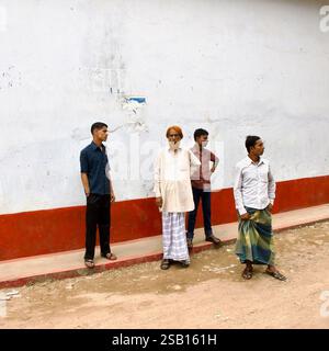 Un homme âgé dans un panjabi et un Lungi se tient avec trois autres contre un mur altéré dans le Sadarghat de Dacca, reflétant la vie quotidienne dans la rue. Banque D'Images