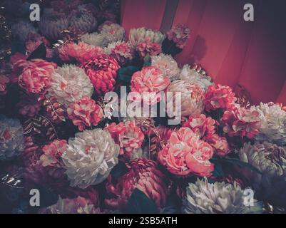 Un gros plan vibrant d'un arrangement luxuriant de fleurs artificielles dans des tons roses et blancs, présentant une esthétique vintage. L'image montre la texture Banque D'Images