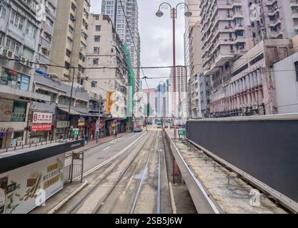 Hong Kong, Chine - 1er février 2025 : Une voie de tramway de Hong Kong descend une rue entre de grands bâtiments par temps couvert. La vue est de Wit Banque D'Images