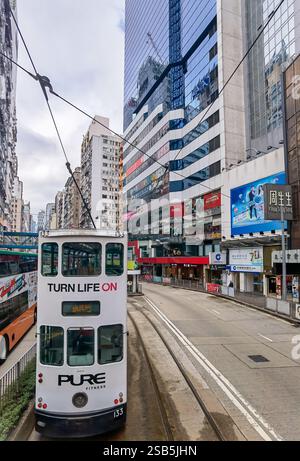 Hong Kong, Chine - 01 février 2025 : Un tramway de Hong Kong, orné de publicité, glisse le long de ses voies dédiées au milieu de bâtiments imposants et Banque D'Images