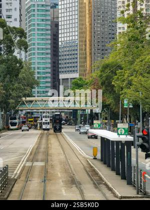 Hong Kong, Chine - 01 février 2025 : Un tramway de Hong Kong glisse le long de ses voies, flanqué de gratte-ciel modernes et de verdure luxuriante. Le paysage urbain Banque D'Images
