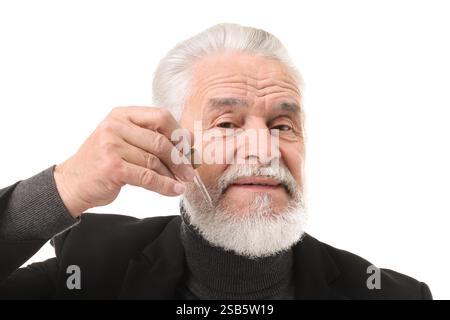Homme senior appliquant le sérum sur sa barbe sur fond blanc Banque D'Images