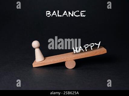 Balance en bois avec une personne d'un côté et les mots équilibrent heureux de l'autre Banque D'Images