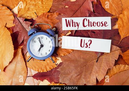 Horloge est sur une pile de feuilles avec les mots pourquoi choisir nous écrit sur un morceau de papier Banque D'Images