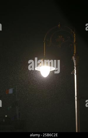 Dublin, Irlande - 28 janvier 2025 - un emblématique lampadaire illuminé de Dublin avec un drapeau irlandais volant en arrière-plan pendant un matin sombre et pluvieux dans la ville de Dublin Banque D'Images