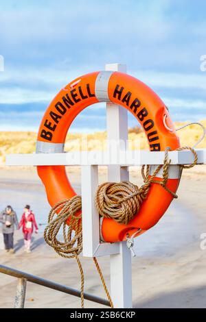 Bouée de sauvetage orange vif stationnée à Beadnell Harbour avec des bâtiments historiques et un ciel bleu en arrière-plan northumberland uk Banque D'Images