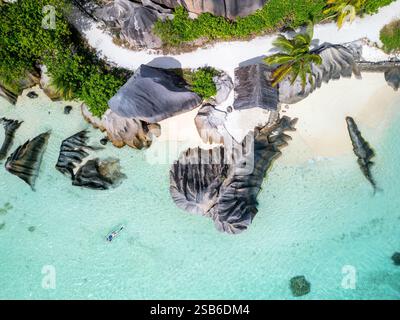 Vue aérienne de l'eau turquoise et des formations rocheuses granitiques uniques à Anse source D'argent, la Digue, Seychelles, avec une femme se relaxant dans un kayak Banque D'Images