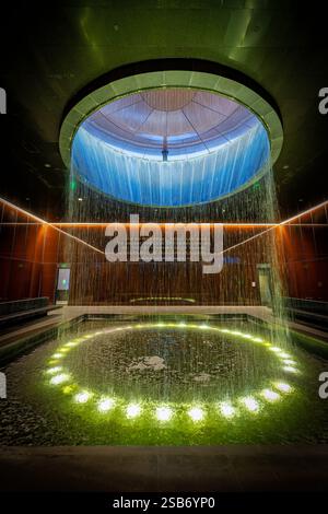 Fontaine de la cour contemplative du Musée national d'histoire afro-américaine à Washington DC | WASHINGTON D.C., États-Unis — illuminée par le bas, la fontaine de la cour contemplative envoie une nappe d'eau à travers un oculus brillant, l'équivalent souterrain du Musée national d'histoire et de culture afro-américaine au Washington Monument qui s'élève juste à l'extérieur. La cour occupe le niveau 0 du hall, le plus profond des étages publics du musée, dans un bâtiment où environ 60 % de la structure se trouve sous le National Mall. Banque D'Images