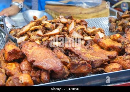 gros plan de tranches de porc frites croustillantes fraîchement cuites exposées sur un stand de marché. La texture brun doré et l'aspect juteux du porc sont salis Banque D'Images