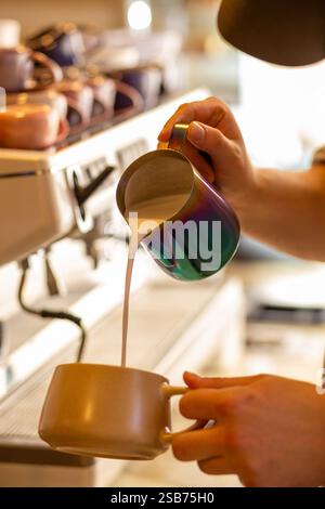 Le barista verse du lait cuit à la vapeur sur du café chaud pour préparer un latte complet Gros plan d'un barista fabriquant du latte art, préparation du café dans un café. Banque D'Images