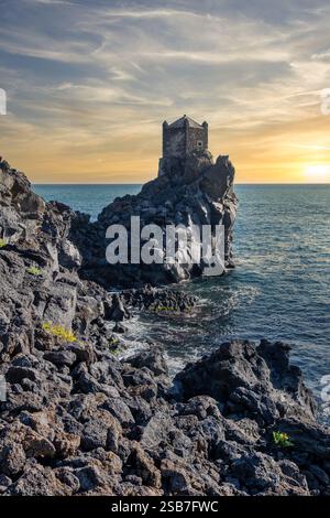 Ancienne tour côtière de Catane, Sicile, debout fièrement au milieu des roches volcaniques accidentées de lave et de la mer Méditerranée bleue profonde sous un SK clair et dynamique Banque D'Images