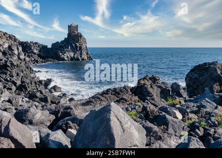 Ancienne tour côtière de Catane, Sicile, debout fièrement au milieu des roches volcaniques accidentées de lave et de la mer Méditerranée bleue profonde sous un SK clair et dynamique Banque D'Images