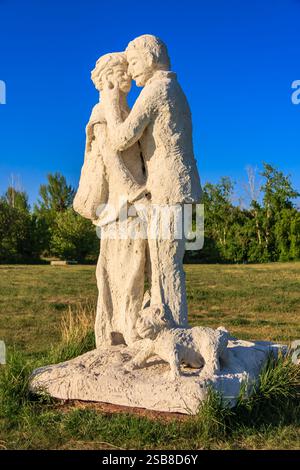 Un couple est représenté dans une sculpture, avec une personne tenant l'autre. La sculpture est blanche et placée dans un champ herbeux. La scène est paisible et rom Banque D'Images