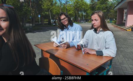 Deux lycéens font une pause à l'extérieur sur le terrain de l'école pour fabriquer des avions en papier à un bureau Banque D'Images