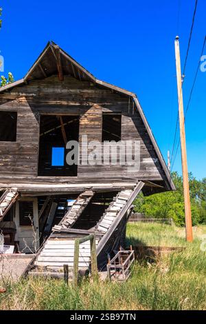 Une vieille grange délabrée avec un poteau qui dépasse du sol. La grange est dans un champ avec de hautes herbes Banque D'Images