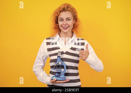 Une femme professeur de biologie scolaire tient un microscope. Femme professeur de biologie. Retour à l'école. Professeur avec microscope isolé sur jaune. Sciences biologiques Banque D'Images
