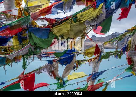 De vieux drapeaux de prière déchirés flottent dans le vent et la neige au-dessus du lac Tilicho. Banque D'Images