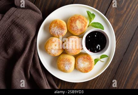 Cheesecakes au fromage cottage (beignets syrniki ou caillé) servis avec de la confiture de myrtilles sur fond de bois. Concept d'alimentation saine. Vue de dessus, plat l Banque D'Images