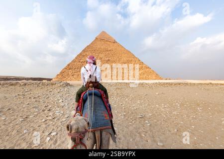 Chameaux dans Gizeh Pyramid Complex - Une femme dans un turban rouge chevauchant un chameau à travers les minces dunes de sable - le Caire, Egypte Banque D'Images