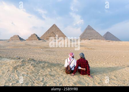 Vue arrière couple amant, touristes femme et homme avec fond de chapeau la pyramide de Gizeh égyptienne, coucher du soleil le Caire, Egypte. Banque D'Images