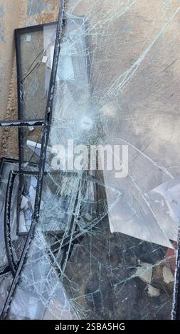Vitres brisées avec cadres noirs, présentant un point d'impact central et des fissures rayonnantes. Les débris reposent sur un fond texturé et bronzé. Banque D'Images