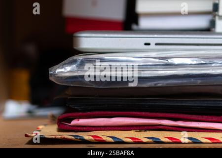 Vue rapprochée d'une pile de divers éléments, y compris un ordinateur portable, des cahiers et des dossiers, disposés sur une surface en bois. Les articles sont superposés avec diffe Banque D'Images