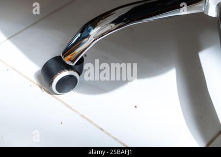 Gros plan d'une roue de chaise de bureau noire et argentée sur un sol carrelé, avec la lumière du soleil projetant des ombres. Banque D'Images