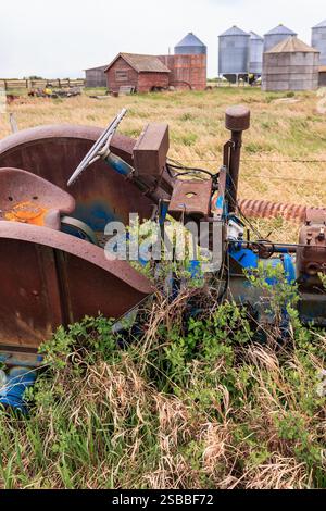 Un vieux tracteur est assis dans un champ avec quelques bâtiments en arrière-plan. Le tracteur est rouillé et il est abandonné Banque D'Images