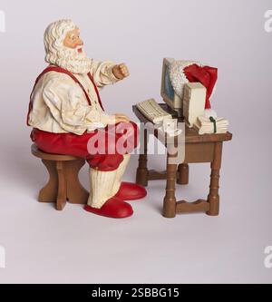 figurine de père noël assis au bureau travaillant sur l'ordinateur faisant la liste de cadeaux des enfants pour noël Banque D'Images