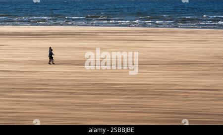 Couple marchant sur la plage avec du sable soufflé, Redcar, Angleterre Banque D'Images