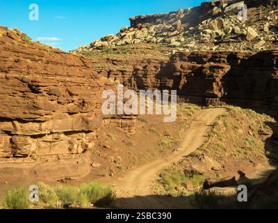 Un canyon rocheux avec un chemin de terre qui le traverse. Le ciel est bleu et le soleil brille Banque D'Images