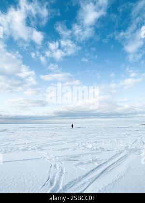 Immense lac gelé couvert de neige épaisse. Paysage marin hivernal : nuages au-dessus de la surface désertique enneigée sans fin avec des empreintes de pas. Banque D'Images