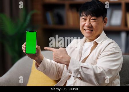 Incroyable application utile, grande offre mobile, publicité mobile, homme excité, homme souriant affichant un smartphone avec un écran vert vierge en position assise Banque D'Images