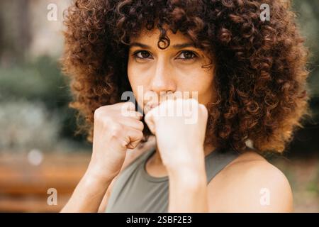Une femme déterminée pratiquant la posture de combat à l'extérieur, montrant la force et la confiance dans un environnement de parc. Banque D'Images