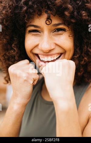 Jeune femme joyeuse sourit joyeusement, posant dans une position de combat à l'extérieur. Son énergie capte l'essence du bonheur et de l'autonomisation. Banque D'Images